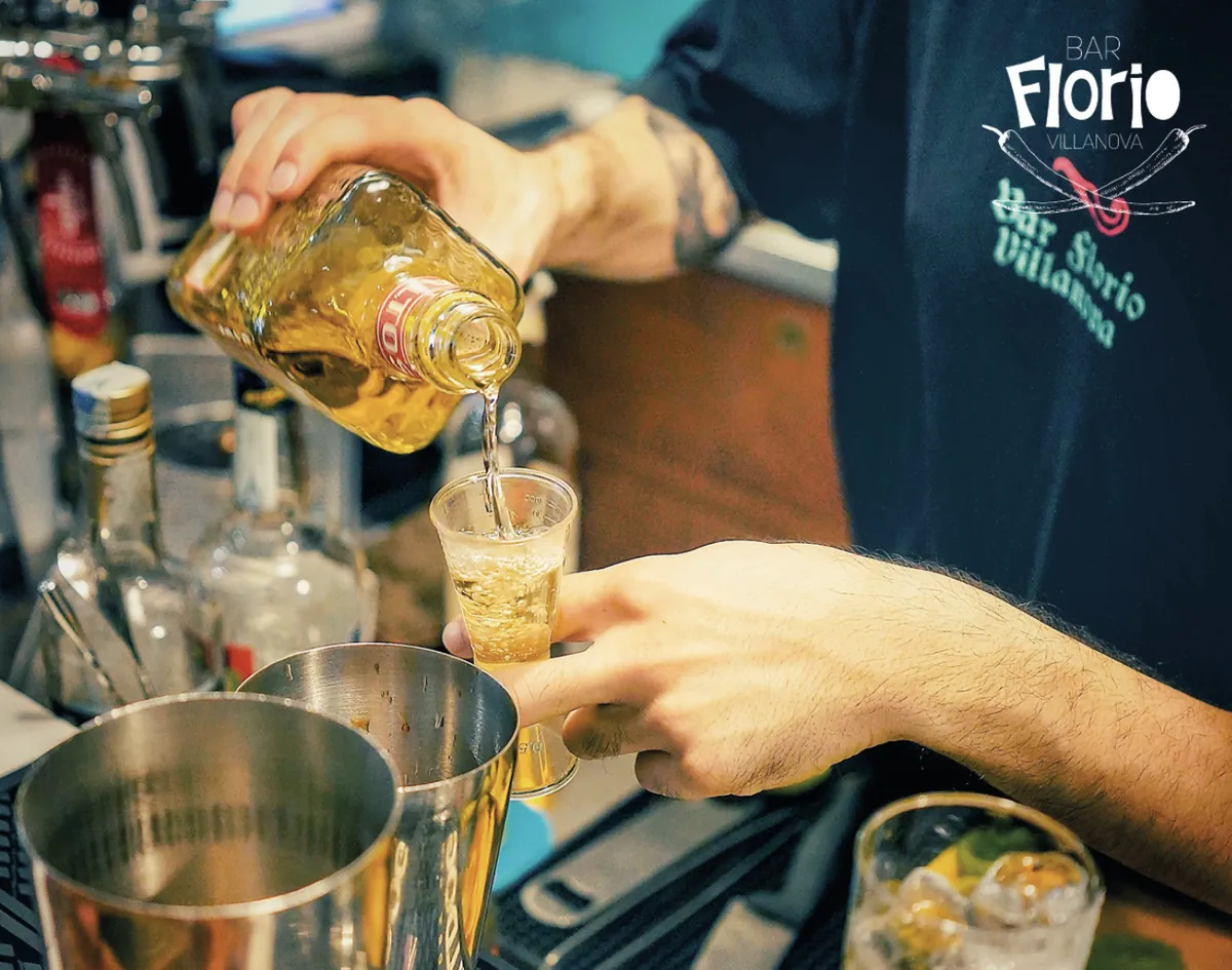 Il barman versa un distillato dentro un misurino dietro al banco del Bar Florio, con la maglietta che porta il marchio del bar